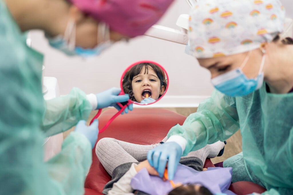 Stock photo of young girl in the dental clinic learning how to clean her teeth with a mirror.